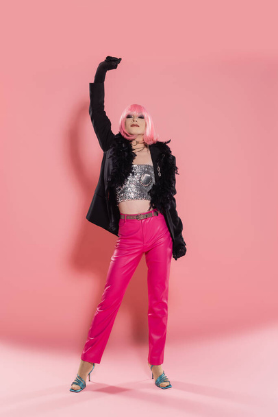Pełna długość stylowej drag queen w kurtce z piórami na różowym tle  - Zdjęcie, obraz