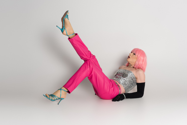 Pessoa transgênero na moda em peruca rosa e top espumante deitado em fundo cinza  - Foto, Imagem