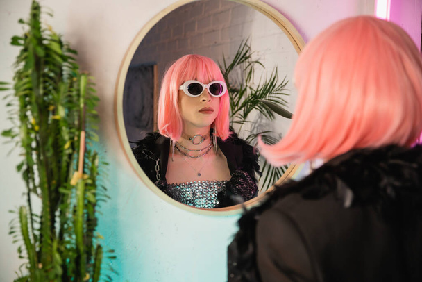 Fashionable drag queen in wig and sunglasses standing near mirror at home  - Foto, immagini