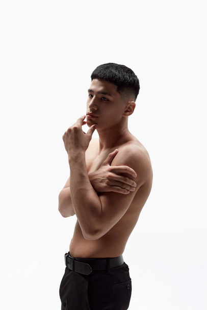 Portrait of asian handsome young man posing shirtless in trousers against white studio background. Spotless face, muscular body. Concept of male beauty, skincare, cosmetology, mens health - Photo, Image
