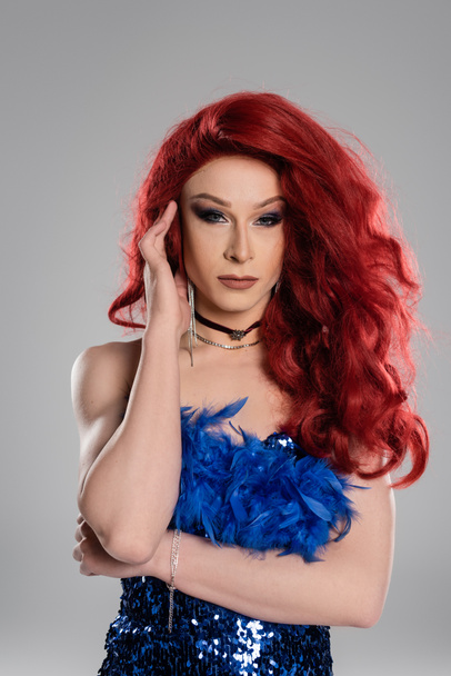 Drag queen in red wig and dress posing and looking at camera isolated on grey  - Photo, Image