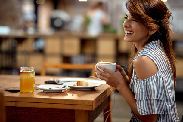 Красивая молодая девушка наслаждается чашкой кофе в одиночестве. Веселая молодая женщина в кафе. Веселье, образ жизни, концепция lesiure. - Фото, изображение