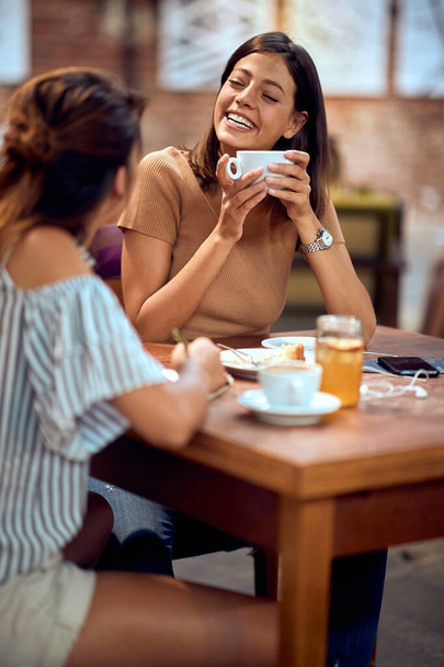 Two happy young woman enjoying coffee together in cafe. Chatting and laughing together. Lifestyle, lesiure, coffee break concept. - Foto, Bild