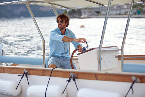 A young handsome man is steering the yacht in the bay on a beautiful sunny day on the seaside. Yacht, holiday, sea - Fotografie, Obrázek