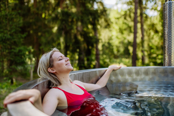 Young woman enjoying wooden bathtub with fireplace to burn wood and heat water in backyard in mountains. - Foto, Imagem