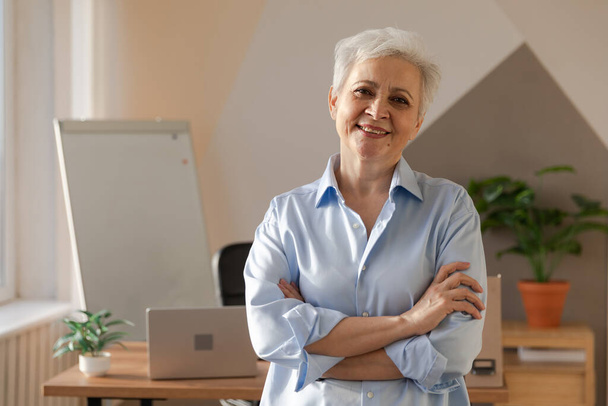 Portrait of confident stylish european middle aged senior woman at workplace. Stylish older mature 60s gray haired lady businesswoman in modern office. Boss leader teacher professional worker - Photo, Image