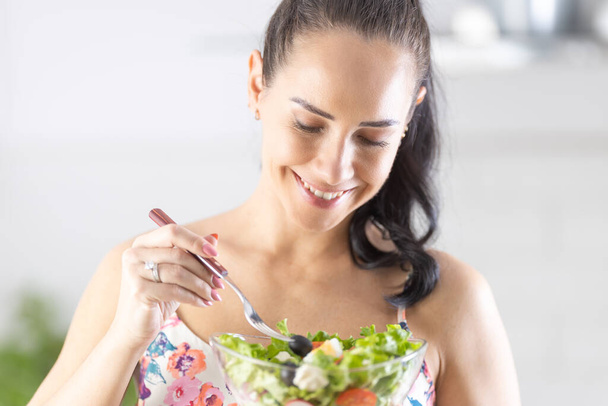 A smiling brunette tastes a healthy salad in her kitchen. - 写真・画像