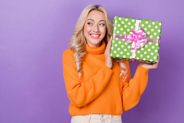 Photo of cheerful girl with stylish hairdo dressed orange sweater arms hold present look empty space isolated on purple color background. - Foto, Bild