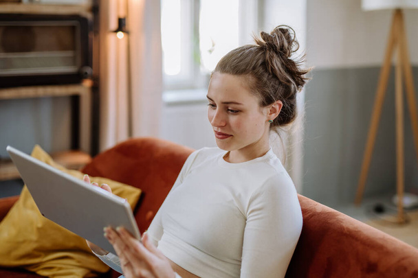 Mujer joven con tableta digital descansando en el apartamento. - Foto, Imagen