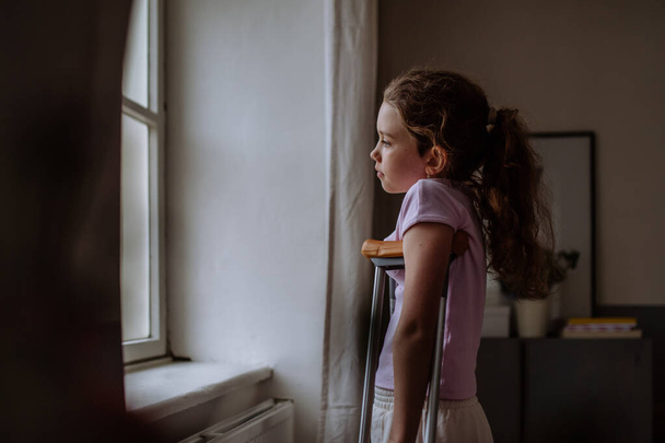 Little girl with broken leg looking trough the window. - Valokuva, kuva