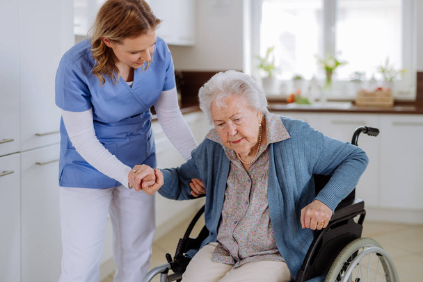 Nurse helping senior woman to stand up from a wheelchair. - Фото, изображение
