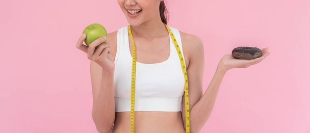 スリムなボディ女性は緑のリンゴとチョコレートドーナツの間に選択し、女性は食事のための緑のリンゴを選択します。健康的な食べ物だ。体重減少,バランス,制御,脂肪を減らす,低カロリー,ルーチン,運動 - 写真・画像