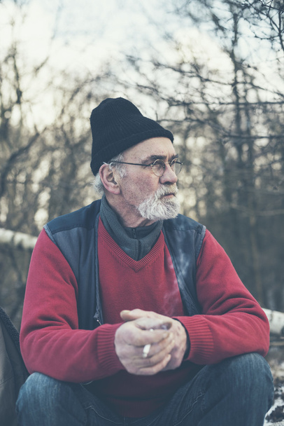 Homem idoso fumando em uma floresta de inverno
 - Foto, Imagem