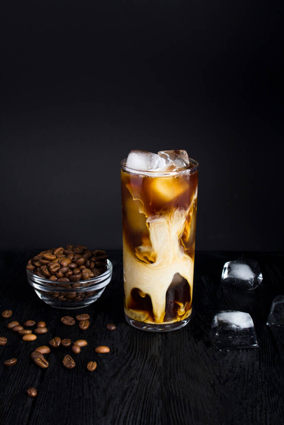 Iced coffee with milk in a tall glass on the dark background. Close-up. Location vertical. - Fotoğraf, Görsel