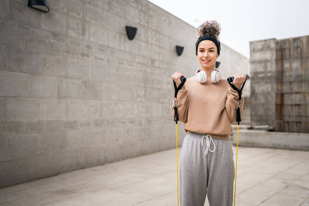 Una donna adulto caucasico atleta femminile formazione con elastici elastici tubi di resistenza all'aperto in città su sfondo di cemento che si estende in felice bruna salute e fitness concetto copiare spazio - Foto, immagini