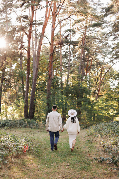 St. Valentines day. Happy stylish loving couple holding hands walking in sunny park. Young bearded man and woman are having date or celebrating anniversary and enjoying each other outdoors. - Photo, Image