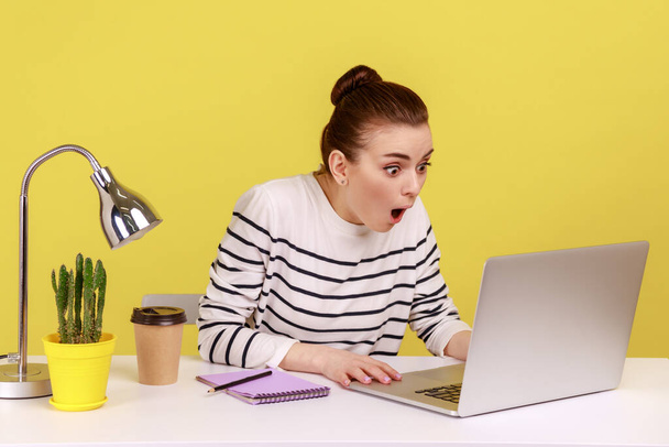 Astonished surprised woman office manager looking at laptop display with big eyes and open mouth, confused with information. Indoor studio studio shot isolated on yellow background. - 写真・画像