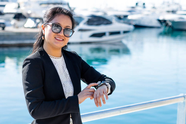 Femme d'affaires asiatique avec des bateaux de luxe en arrière-plan pointant vers l'horloge. - Photo, image