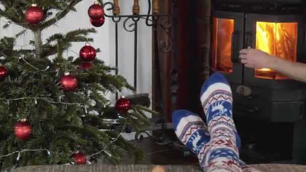 Lazíts a kandalló melletti kanapén. Karácsonyfa és kandalló. Egy karácsonyi zoknis lány lábai.. - Felvétel, videó