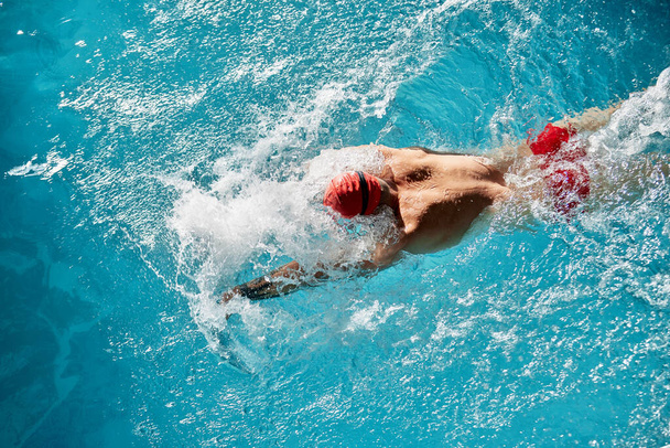 Natation - natation masculine brasse. Gros plan portrait d'un homme faisant un AVC du sein nageant dans une piscine portant un bonnet de bain rouge et des lunettes de bain. - Photo, image