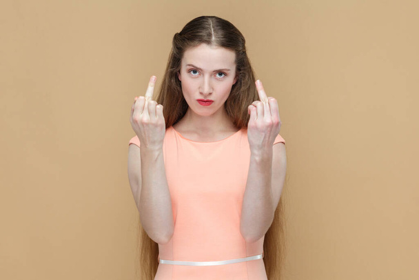 Portrait of rude impolite attractive pretty woman with long hair showing middle finger, arguing with somebody, wearing elegant dress. Indoor studio shot isolated on brown background. - 写真・画像