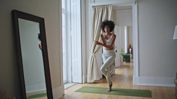 Modelo delgado practicando yoga asana en la esterilla. Mujer africana en forma haciendo namaste pose ejercicio en la alfombra. Flexible balanza de entrenamiento de dama rizada meditando en la habitación blanca. Armonía concepto de estilo de vida activo - Imágenes, Vídeo