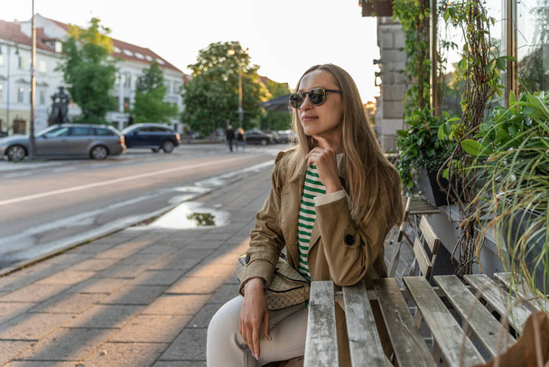 Una donna si siede a un tavolo di legno in un caffè di strada in occhiali da sole. - Foto, immagini