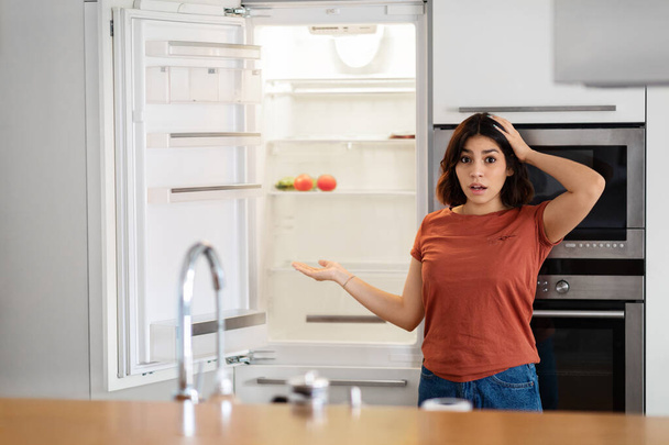 Shocked Young Arab Woman Near Empty Fridge With No Food At Home, Confused Middle Eastern Female Opening Refrigerator And Touching Head, Hungry Lady Suffering Financial Crisis, Copy Space - Fotó, kép