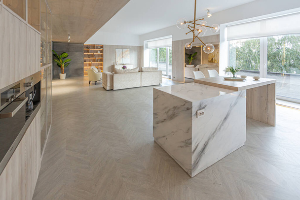 trendy modern interior design of a large studio in white and beige colors with large floor to ceiling windows. area of white kitchen with an island and a recreation area - Fotó, kép