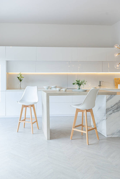luxury interior design of modern trendy snow white kitchen in minimalistic style with island and two bar stools. huge windows to the floor and a glass rack for dishes - Photo, Image