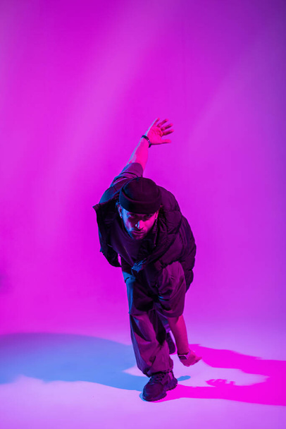 Cooler Trendmann professioneller Tänzer in schwarzer Modekleidung tanzt in rosa und Neonlicht im Studio - Foto, Bild