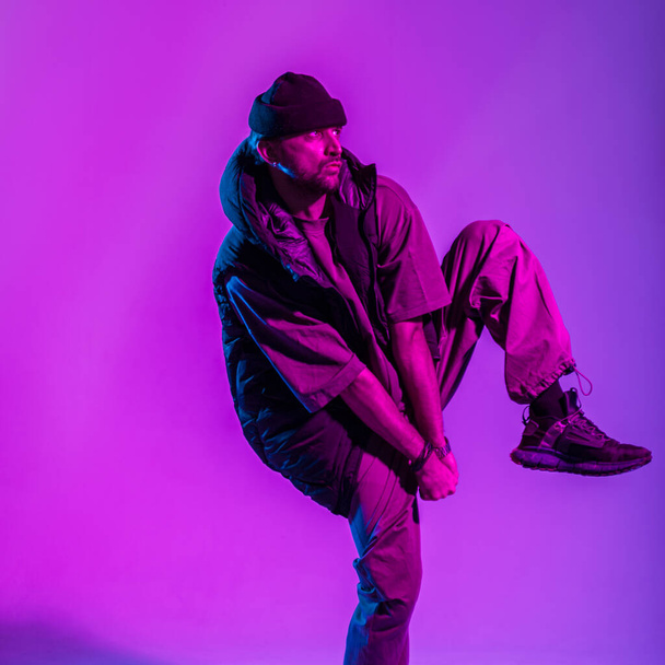 Μοντέρνος νέος επαγγελματίας χορευτής άντρας με ρούχα μόδας χορεύει σε πολύχρωμο στούντιο με δημιουργικό ροζ και νέον φως - Φωτογραφία, εικόνα