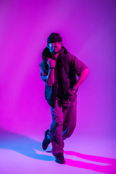 Cool hipster χορευτής άνθρωπος σε μοντέρνα μαύρα ρούχα χορό στο στούντιο με ροζ και νέον φώτα - Φωτογραφία, εικόνα