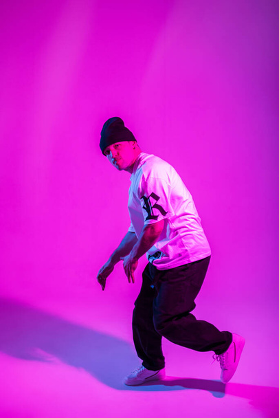 Stylish breakdancer man in fashion clothes with sneakers dancing in studio with pink and neon lights - Photo, Image