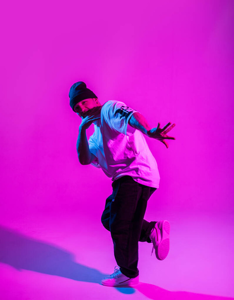 Handsome professional break dancer guy in trendy fashion clothes dancing in creative studio with pink and neon light - Fotó, kép