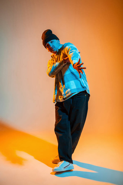 Κομψό όμορφο μόδα b-boy χορευτής τύπος σε μοντέρνα ρούχα ποζάρουν στο στούντιο με πορτοκαλί και μπλε χρώμα - Φωτογραφία, εικόνα