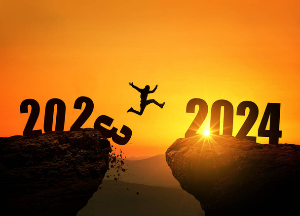 Uomo che salta sulla scogliera 2024 sopra il precipizio con pietre al tramonto stupefacente. Il concetto di anno nuovo. 2023 cade nell'abisso. Benvenuto 2024. La gente entra nell'anno 2024, idea creativa. - Foto, immagini