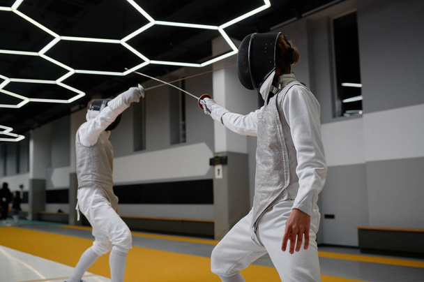 Athletes in uniforms and protective helmet mask fighting duel with rapiers. Swordsmanship competition concept. Martial art - Photo, Image