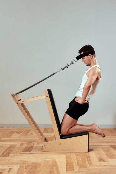 Мужчина делает упражнения для шеи на реформаторах во время пилатеса, юноша показывает упражнения для шейного отдела позвоночника во время пилатеса на реформаторах - Фото, изображение