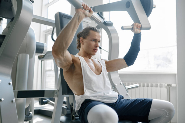 Energetic masculine sportsman working arms pumping muscles on training apparatus at sport gym - Fotoğraf, Görsel