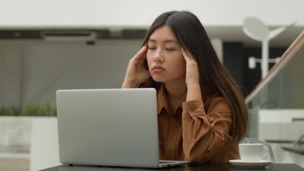 Exhausted overworked Asian chinese japanese woman student girl studying online with laptop in cafe tired sick businesswoman think difficult decision thought suffer headache massage temples pain head - Footage, Video