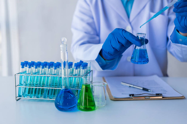 Medische of wetenschappelijke onderzoeker of mannelijke arts op zoek naar reageerbuis van transparante oplossing in laboratoriumanalyse reageerbuis met blauwe vloeistof in het laboratorium - Foto, afbeelding