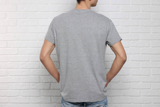 Man wearing gray t-shirt near white brick wall, back view. Mockup for design - Photo, Image