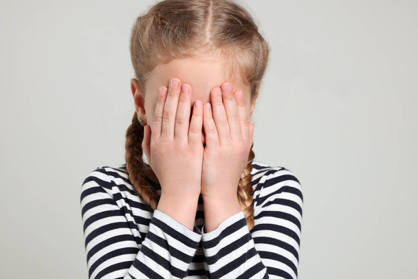 Girl covering face with hands on light grey background. Children's bullying - 写真・画像