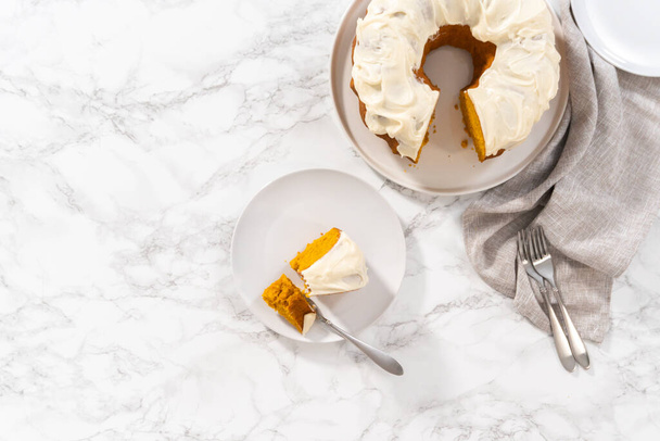 Acostado. Rebanada de pastel de calabaza casera con glaseado de queso crema en un plato blanco. - Foto, imagen