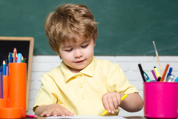 Cute little preschool kid boy study in a classroom. Cheerful smiling little boy Pupil having fun against blackboard. Cheerful smiling child at the blackboard - Foto, afbeelding