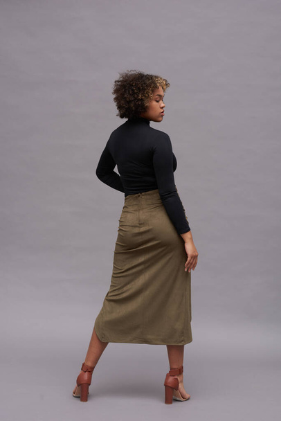 Rear view of young African American stylish woman in turtleneck and long skirt standing in front of camera in studio and looking aside - Fotoğraf, Görsel