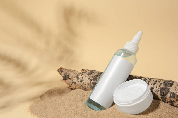 Cosmetic products and tree bark on sand against beige background. Space for text - Foto, Bild
