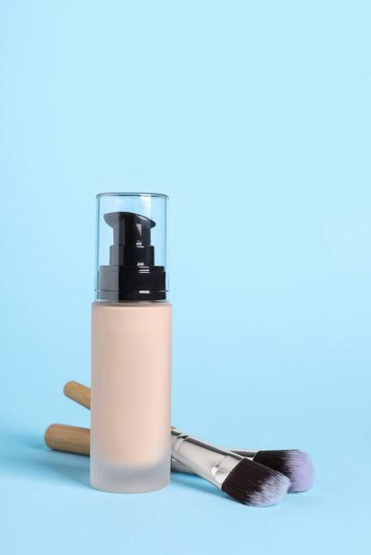Bottle of skin foundation and brushes on light blue background. Makeup product - 写真・画像