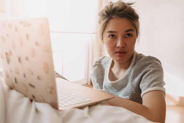Serious asian woman working with her laptop in the bedroom. - Valokuva, kuva